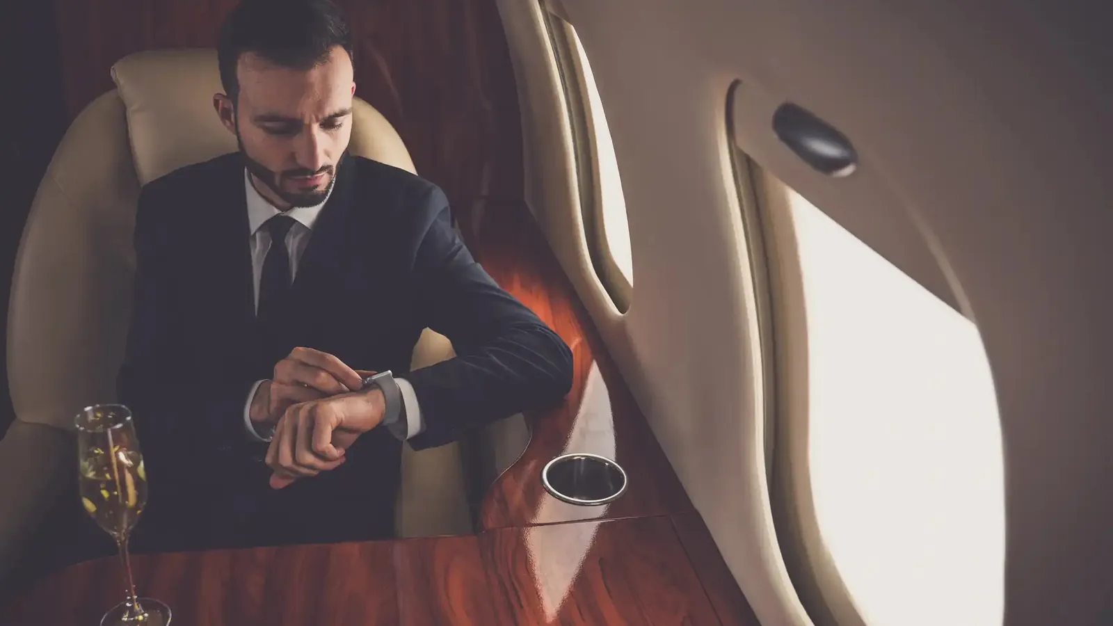 Kabinentisch eines Business Jets mit Laptop und Unterlagen, vor den Fenstern Wolken über den Alpen