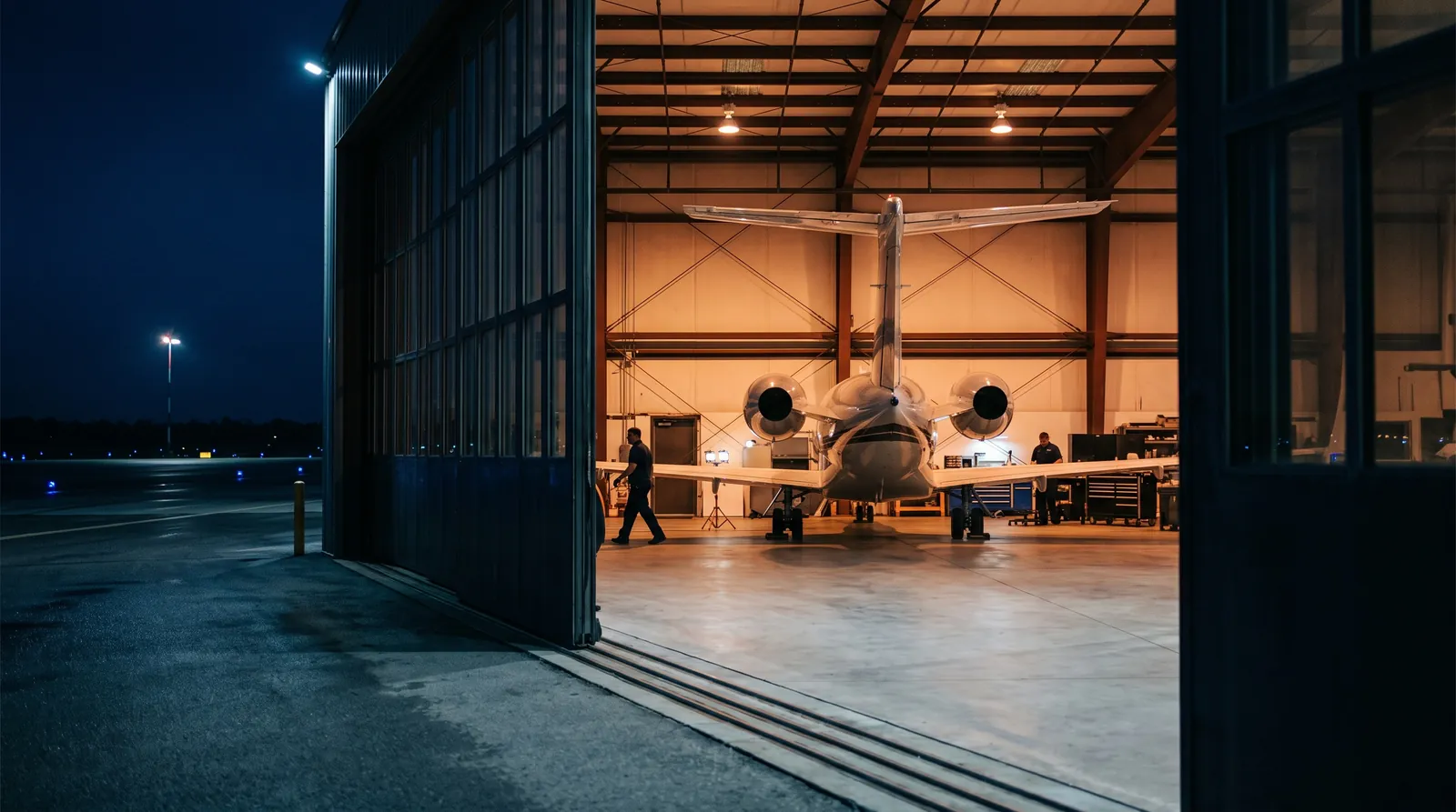 Ein Privatjet in einem beleuchteten Hangar, durch ein halb offenes Tor gesehen